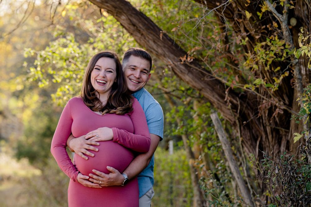 A couple embraces during their maternity photoshoot on a nature trail with golden sunlight.