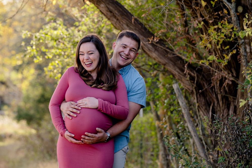 A couple shares a laughing moment during their maternity photography session in a park.