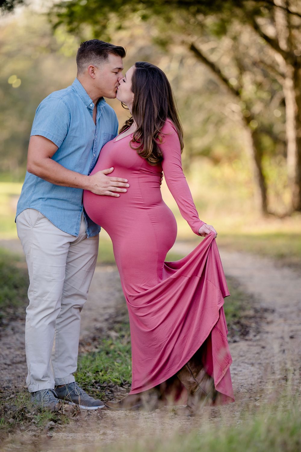 A couple shares an intimate moment during their maternity photoshoot on a nature path.