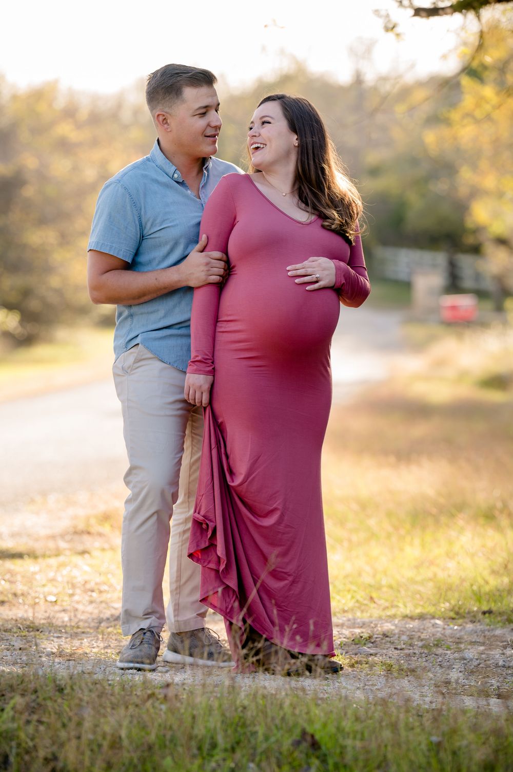 A couple shares a joyful moment together during a maternity photoshoot in golden sunlight.