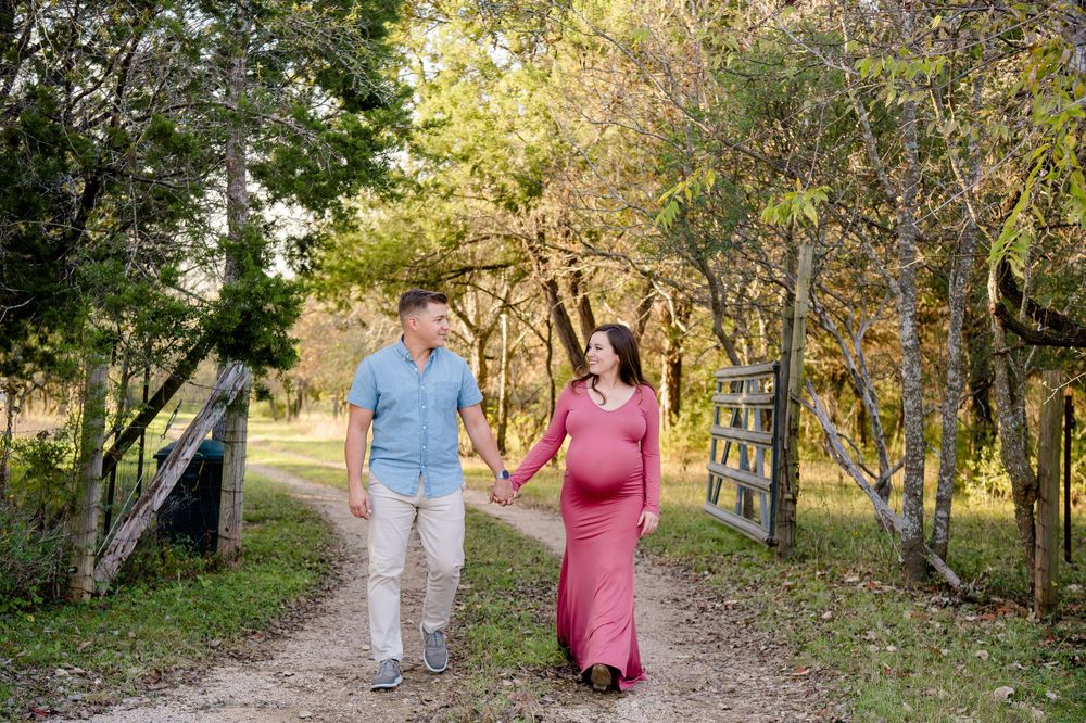 A couple walks hand in hand down a tree-lined path during their maternity photo session.