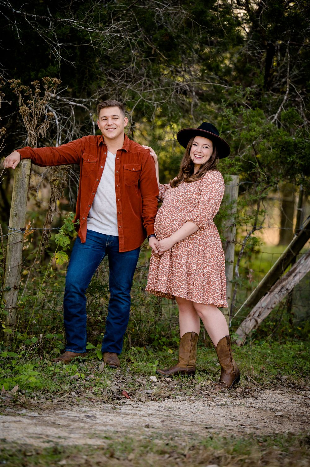 Expectant couple in casual western wear poses together on woodland path.