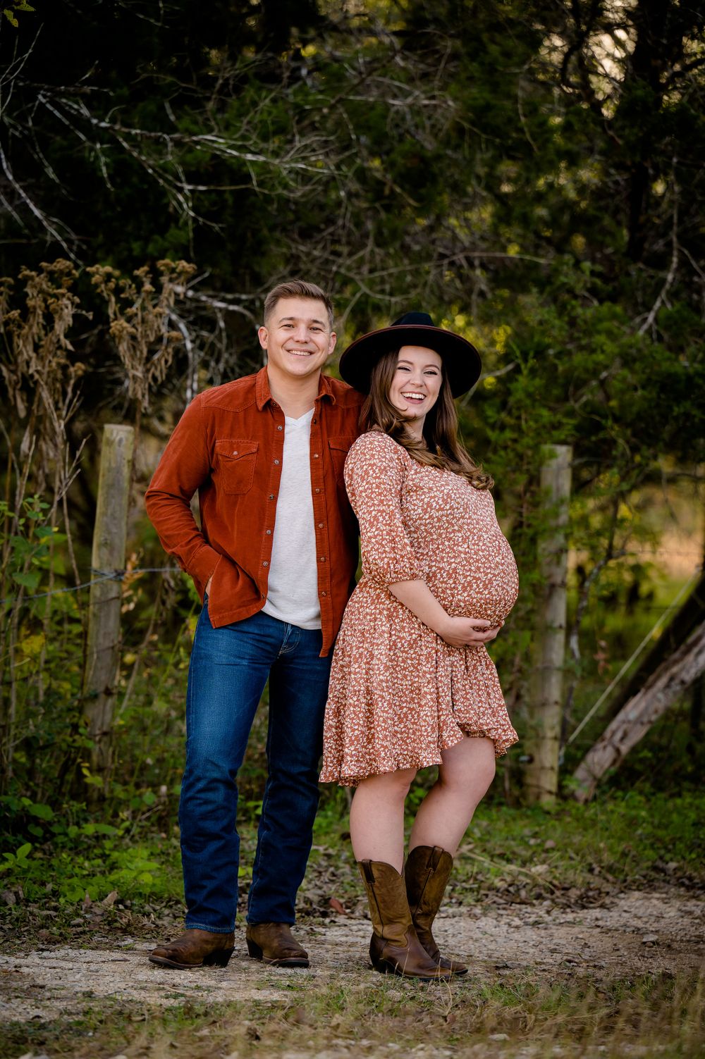 Couple poses outdoors in autumn setting with floral dress and rustic attire during maternity photoshoot.