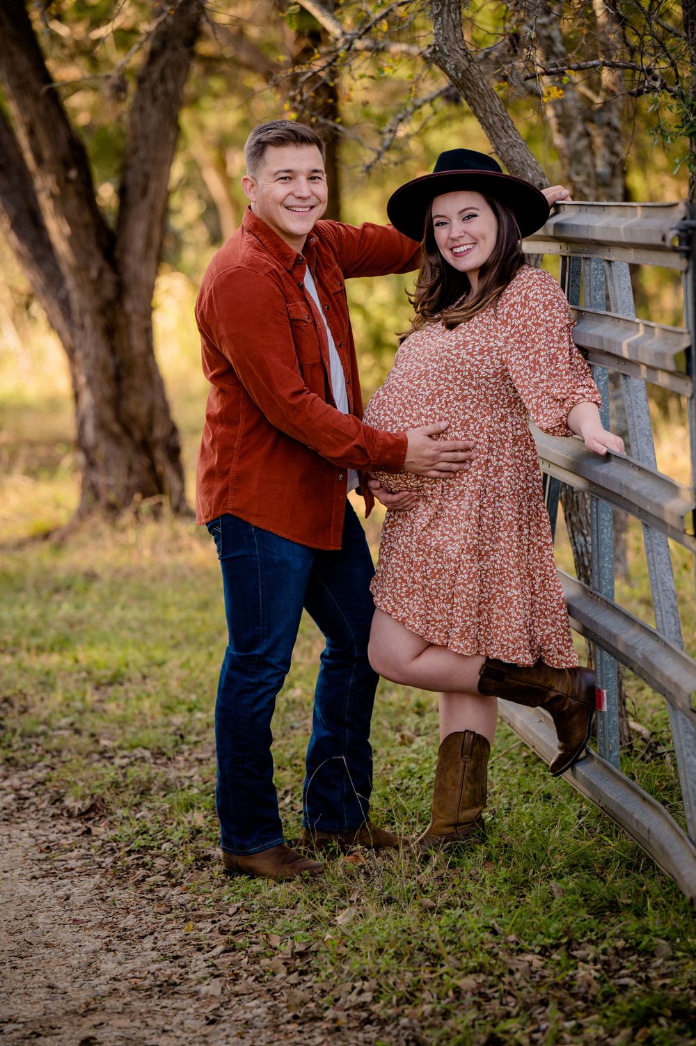 Maternity photo of couple by wooden fence wearing rustic attire in autumn woodland setting.