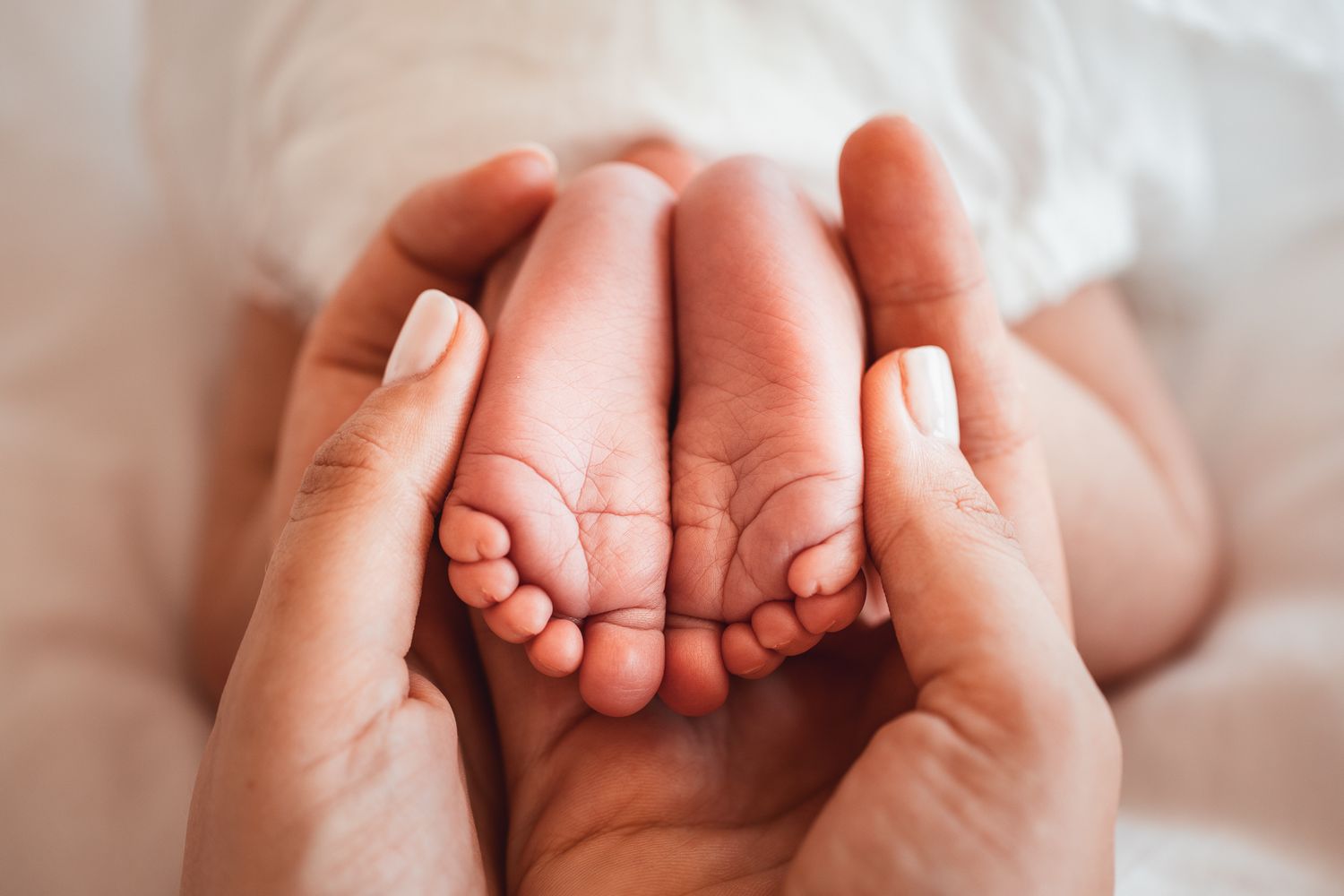 Tiny newborn feet held gently in caring hands against white background.