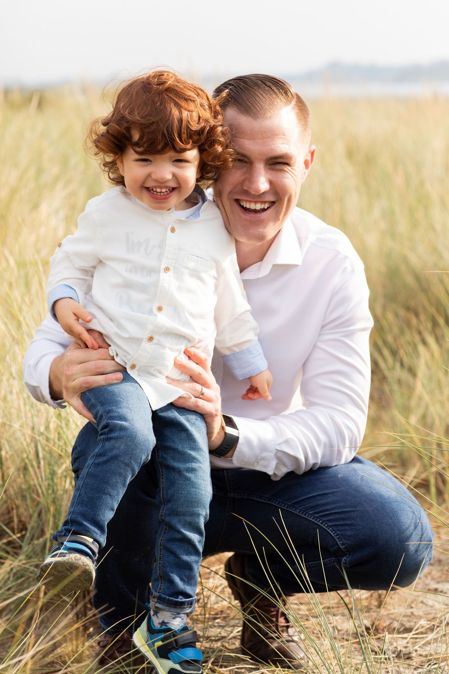 A pair share joyful laughter while sitting in tall grass on a sunny day.