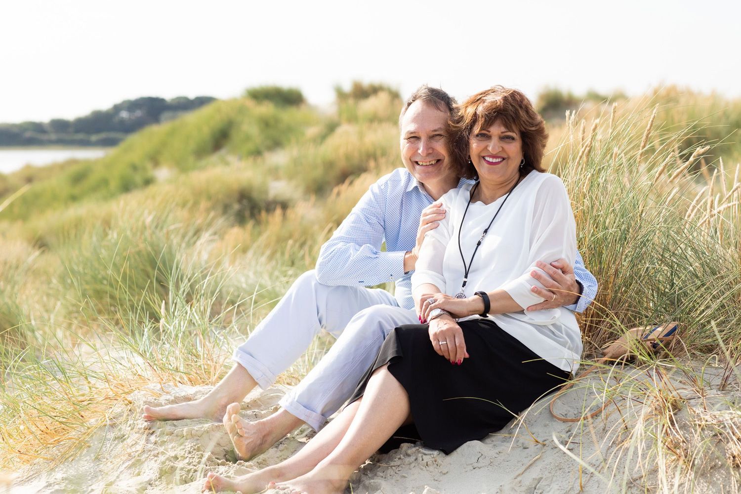 A couple sits relaxing together in coastal sand dunes on a sunny day.