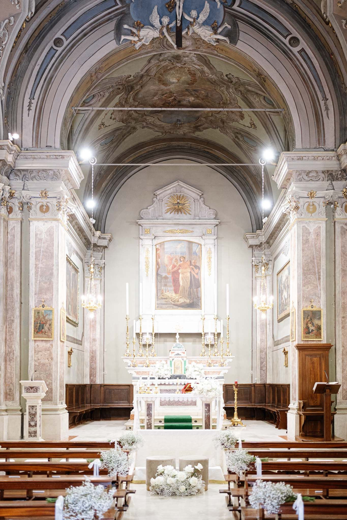 Ornate Italian church interior with baroque architecture and white floral wedding decorations.