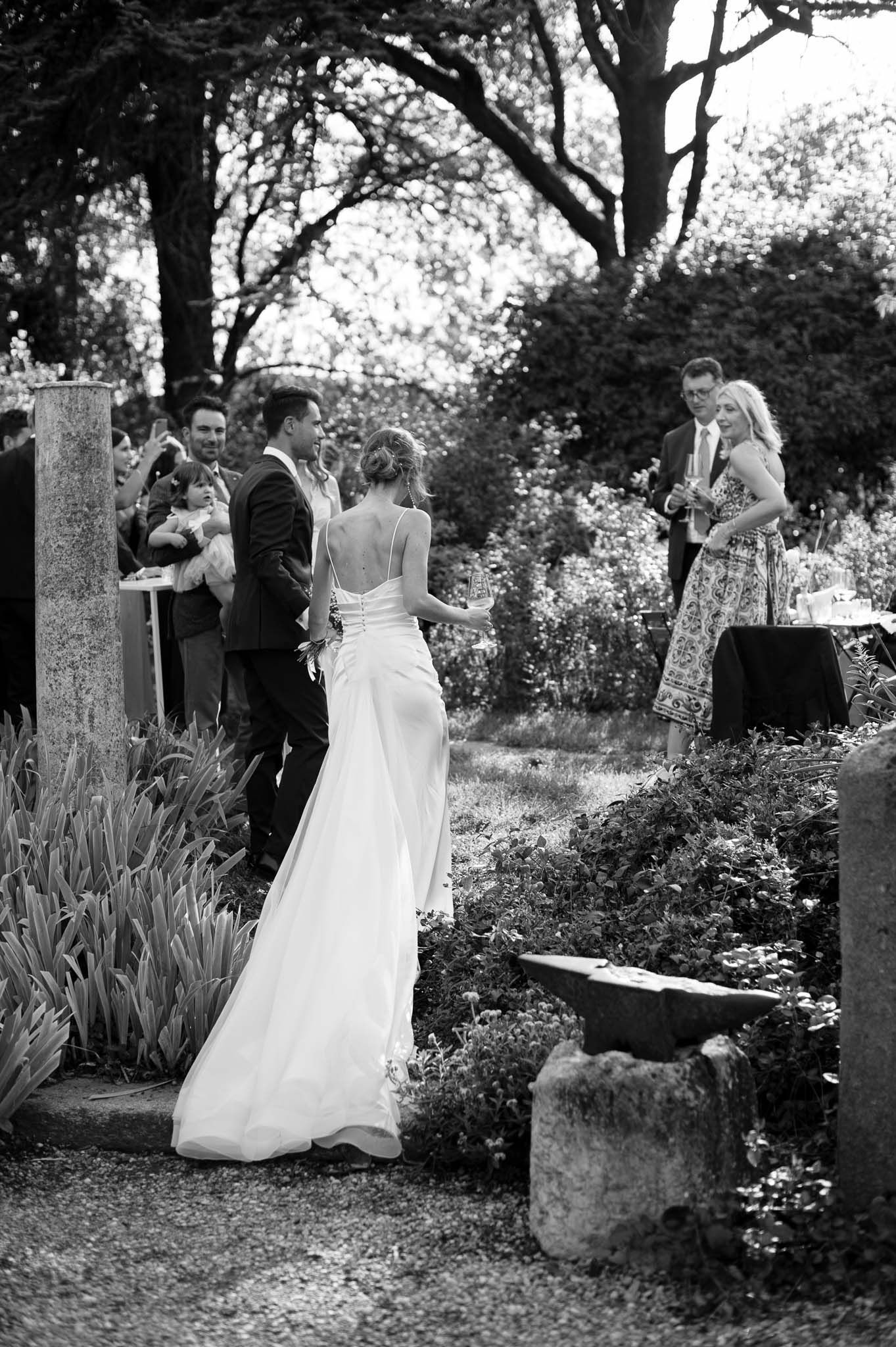 Black and white outdoor wedding ceremony in a garden setting with stone pillars and greenery.