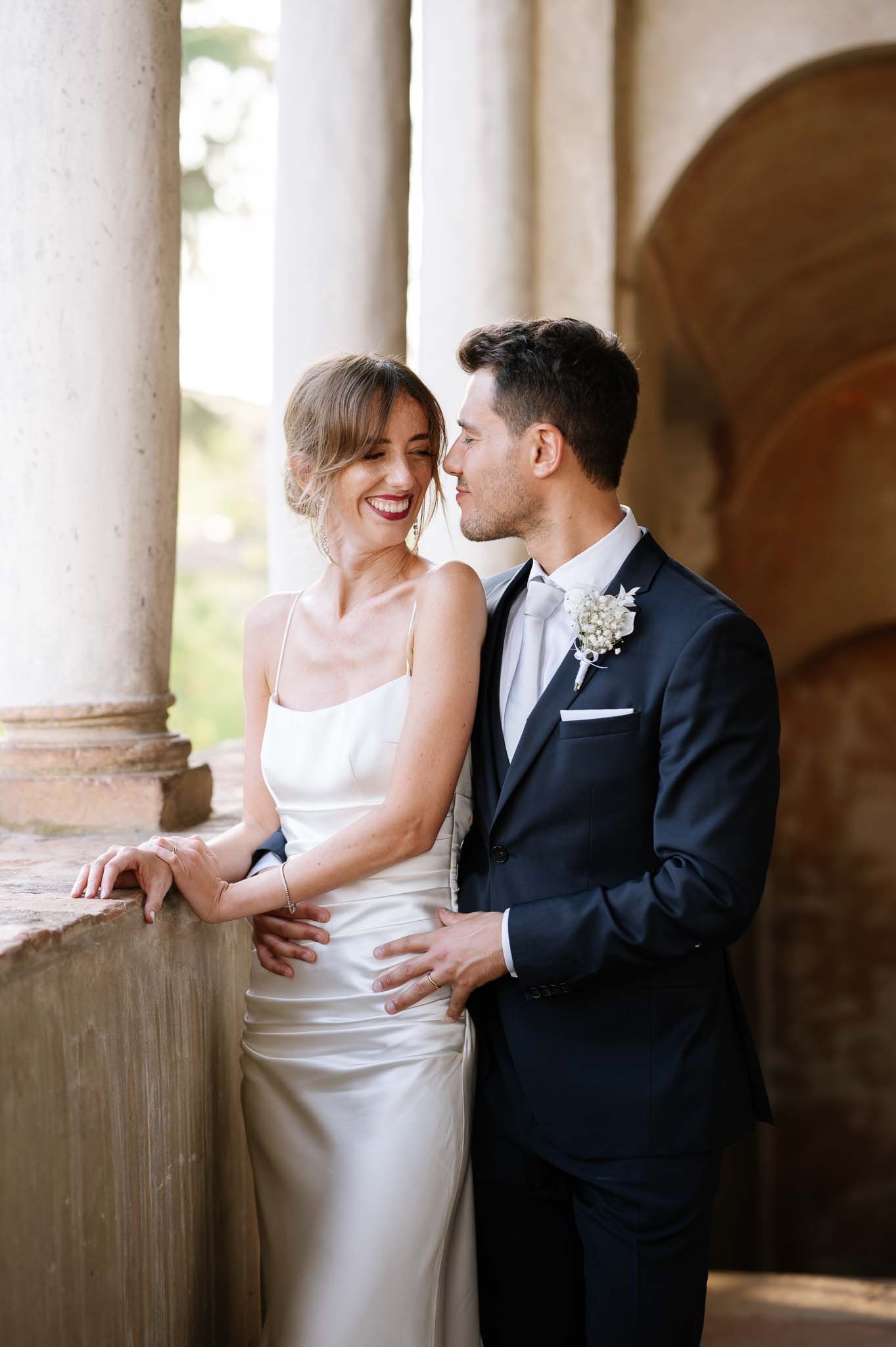 Romantic wedding couple embracing in an elegant colonnade with natural light.