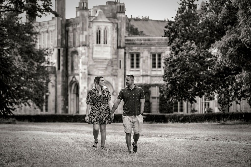 A couple walking hand in hand in front of a grand historic building.