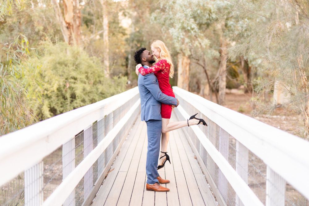 Romantic couple embracing on wooden boardwalk in elegant attire.