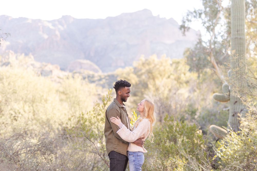 Couple embracing in desert landscape with mountains and natural scenery in background.