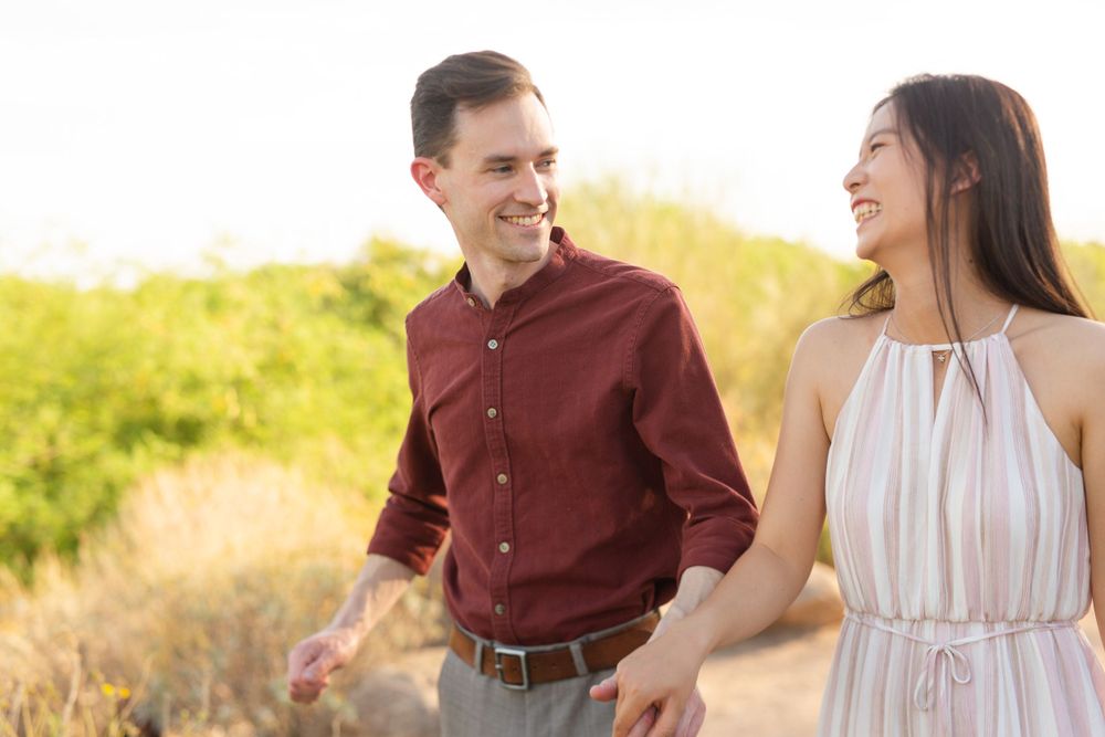 A couple walking together in a golden field during sunset wearing casual dressy attire.