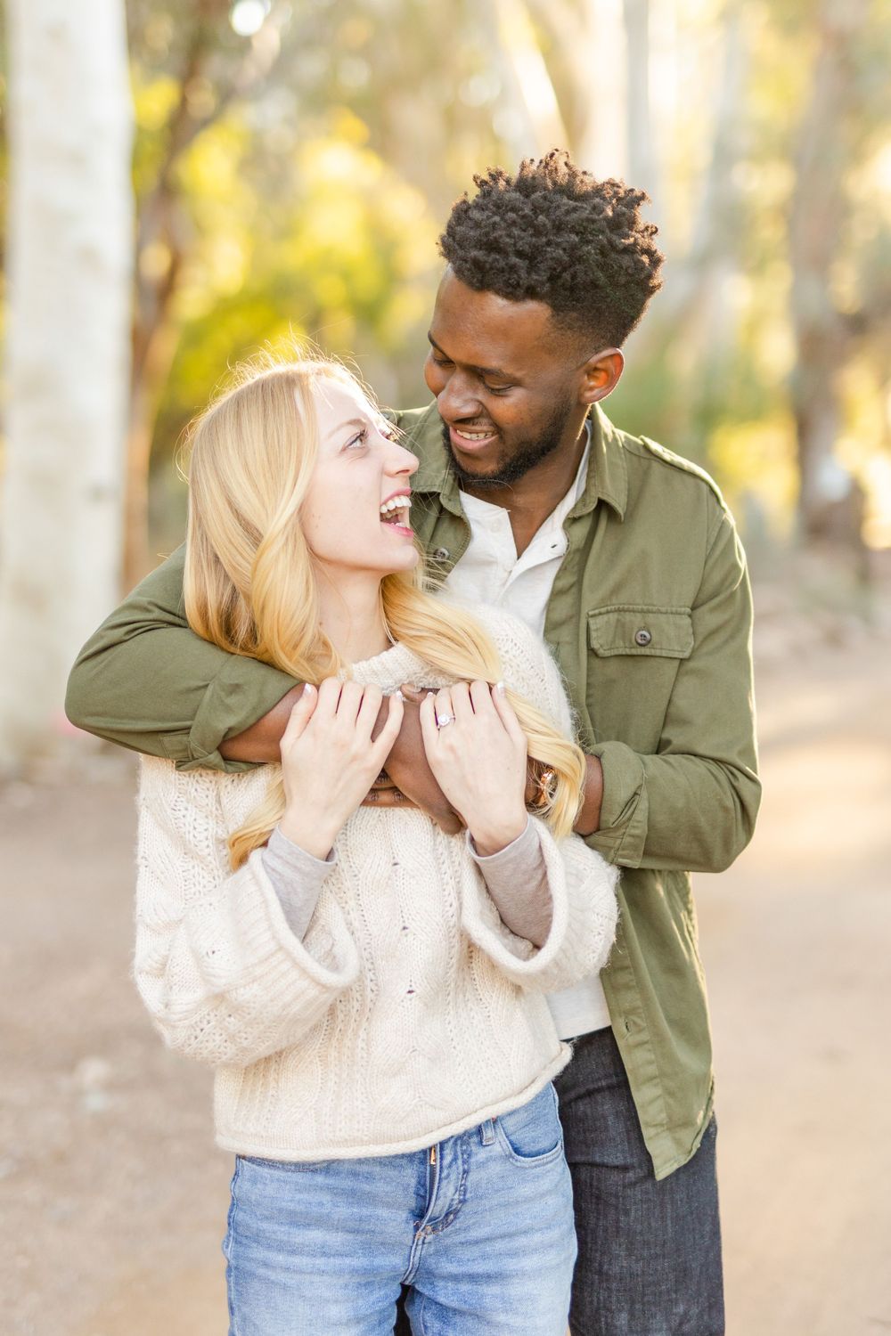 Happy couple laughing and embracing in a wooded area with warm autumn lighting.
