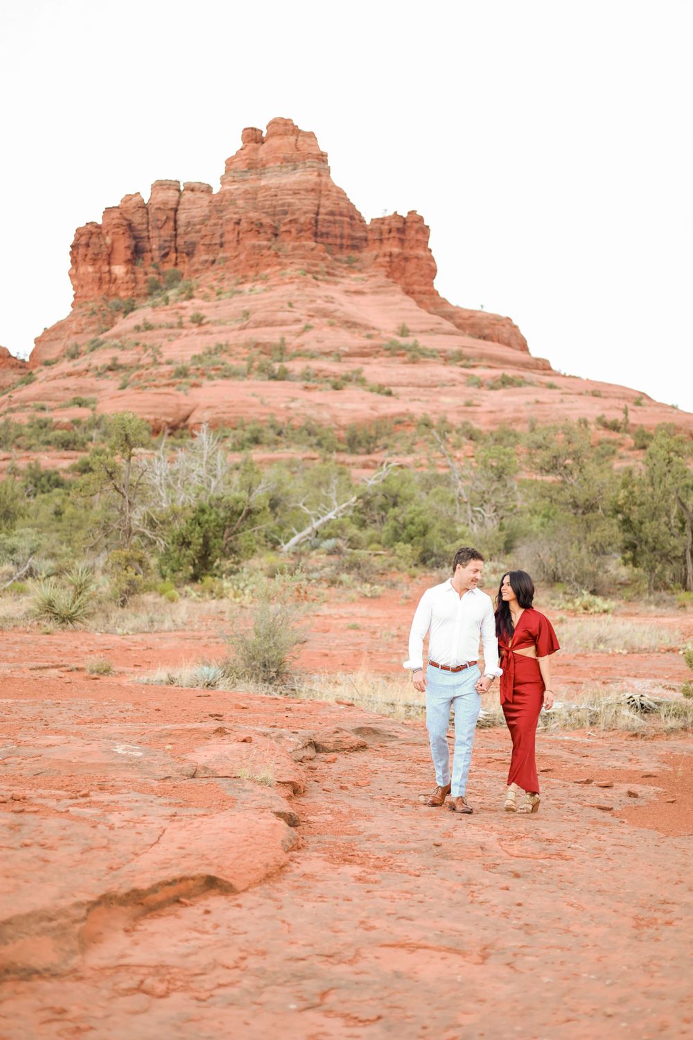 A couple walks together near a majestic red rock formation in Sedona.