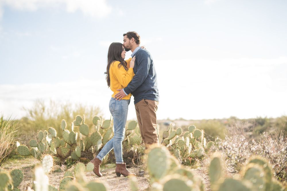 Couple sharing an intimate moment among desert cactus plants at sunset.