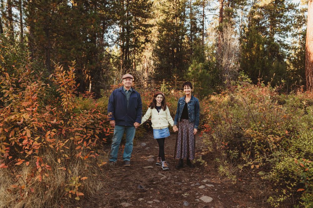 A family walks along an autumn trail surrounded by colorful foliage and evergreen trees.