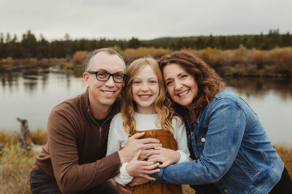 Family of three shares intimate moment by lake during autumn season.