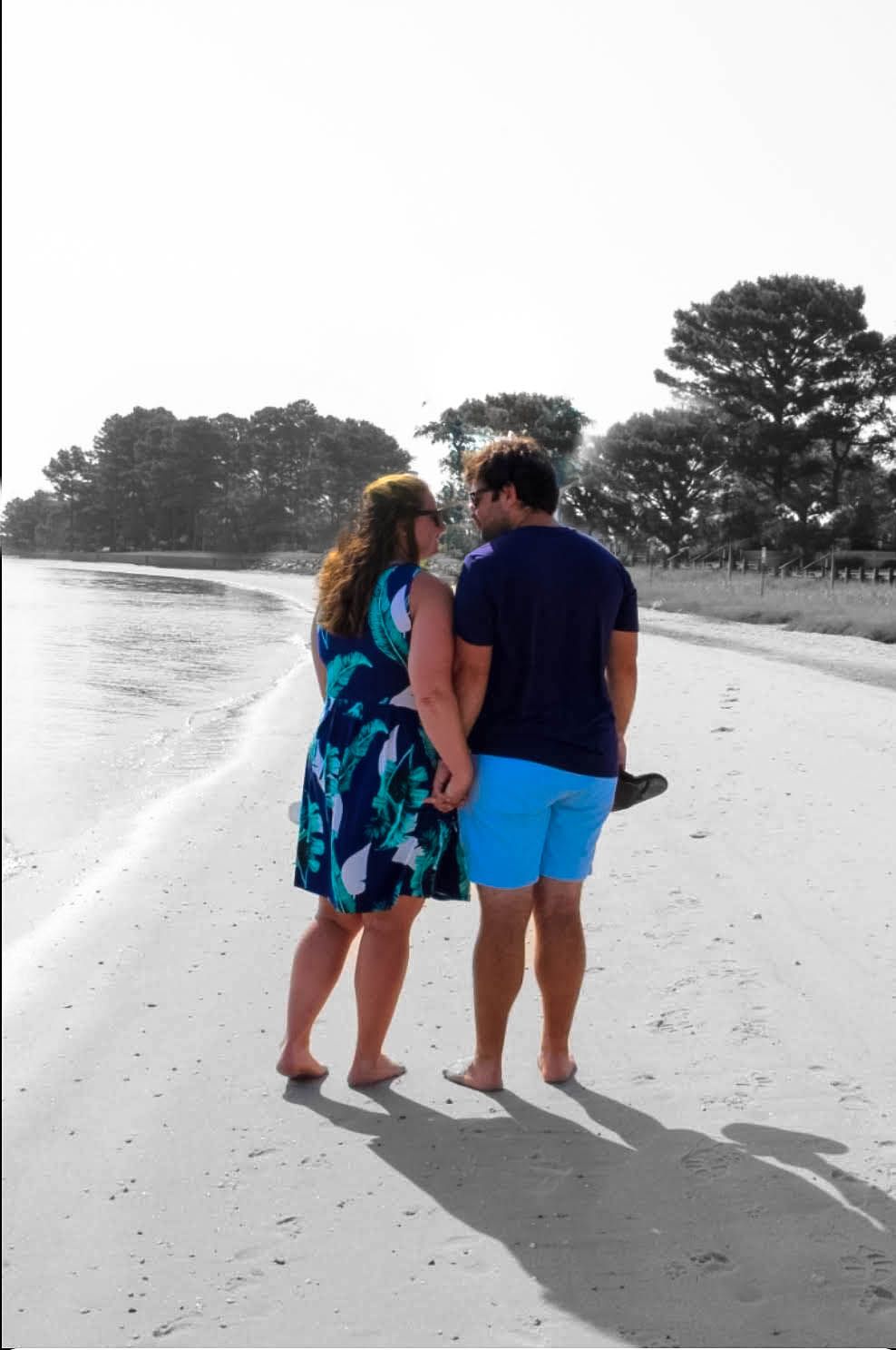 A couple walking together on a beach in black and white photography with selective color.