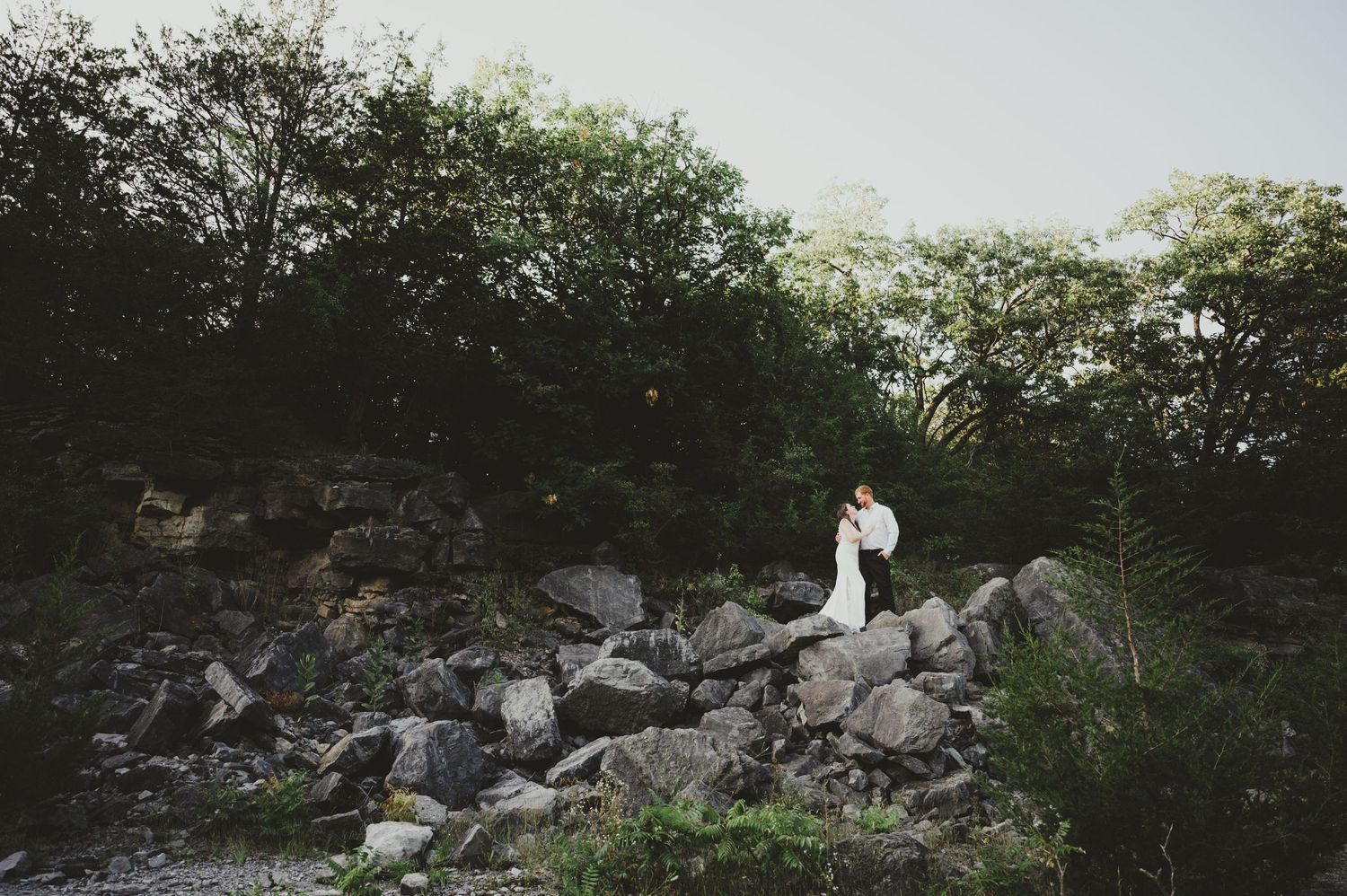A white dress flows in the wind against a rocky natural backdrop with green foliage.