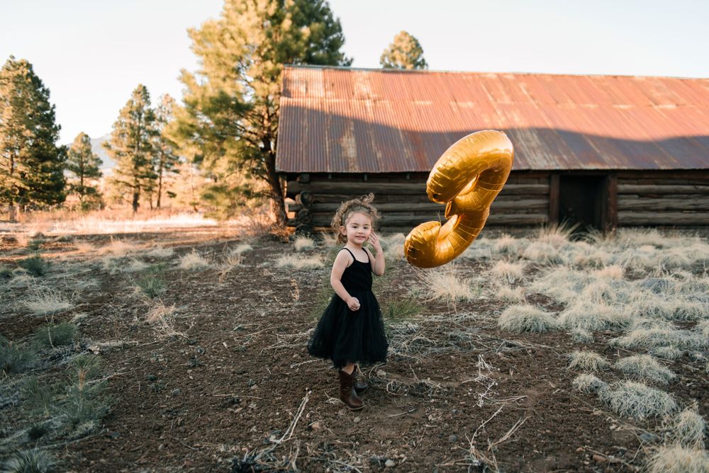 A person poses with a metallic gold number 9 balloon in front of trees during golden hour.