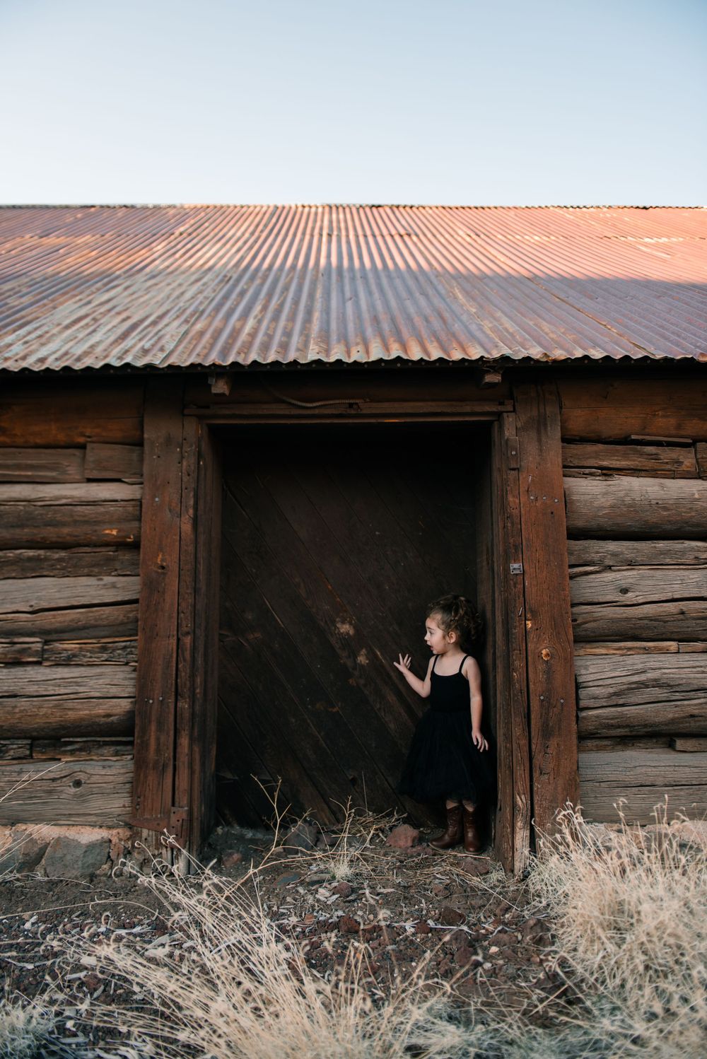 A dark silhouette appears in the doorway of an old wooden barn with a corrugated metal roof.