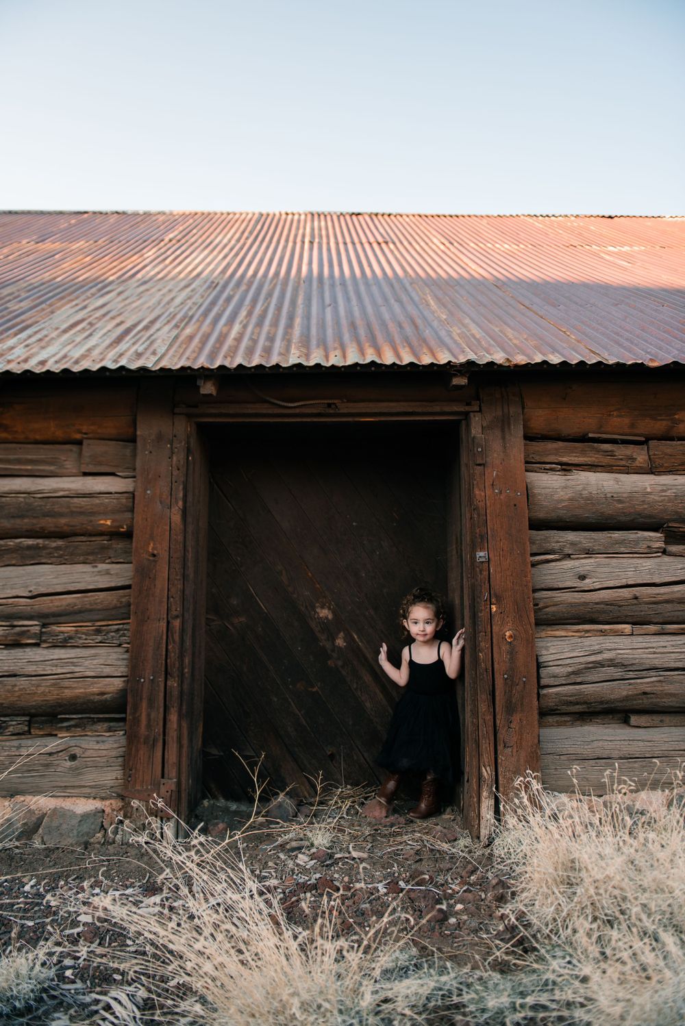 A person peeks through the doorway of an old wooden structure at sunset.