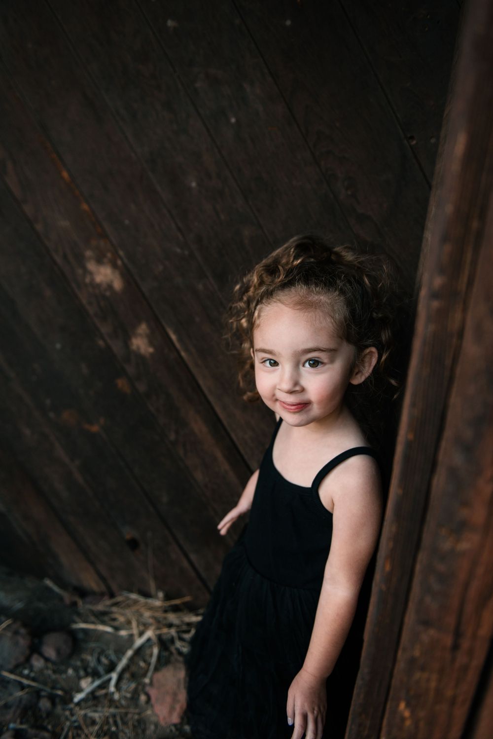 A small figure in a black dress stands against dark wooden planks.