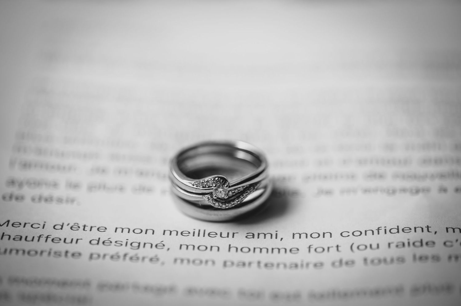 Close-up black and white photo of a diamond engagement ring and wedding band on printed text paper.