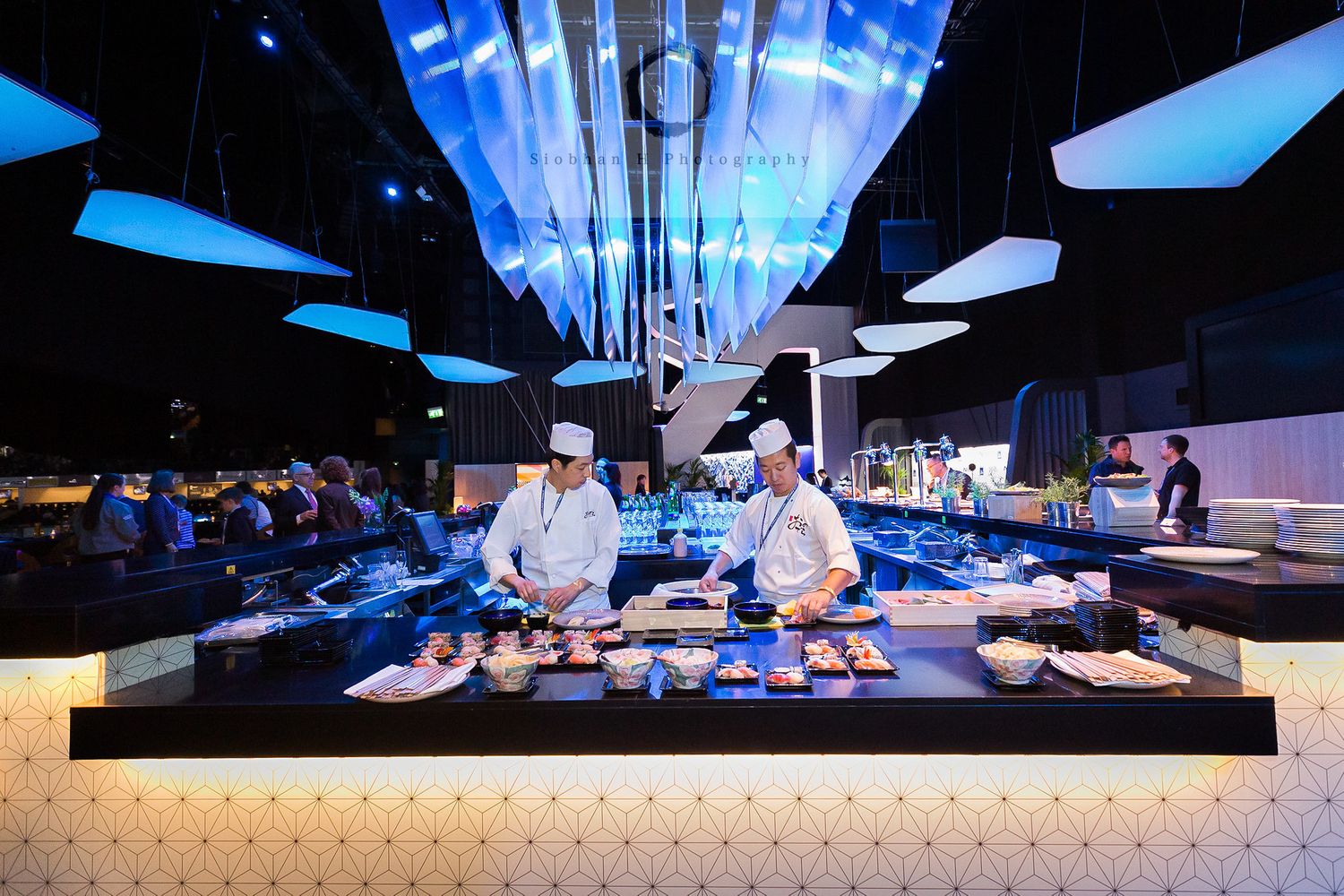 Chefs preparing food at an elegant event with dramatic blue lighting and multiple serving stations.