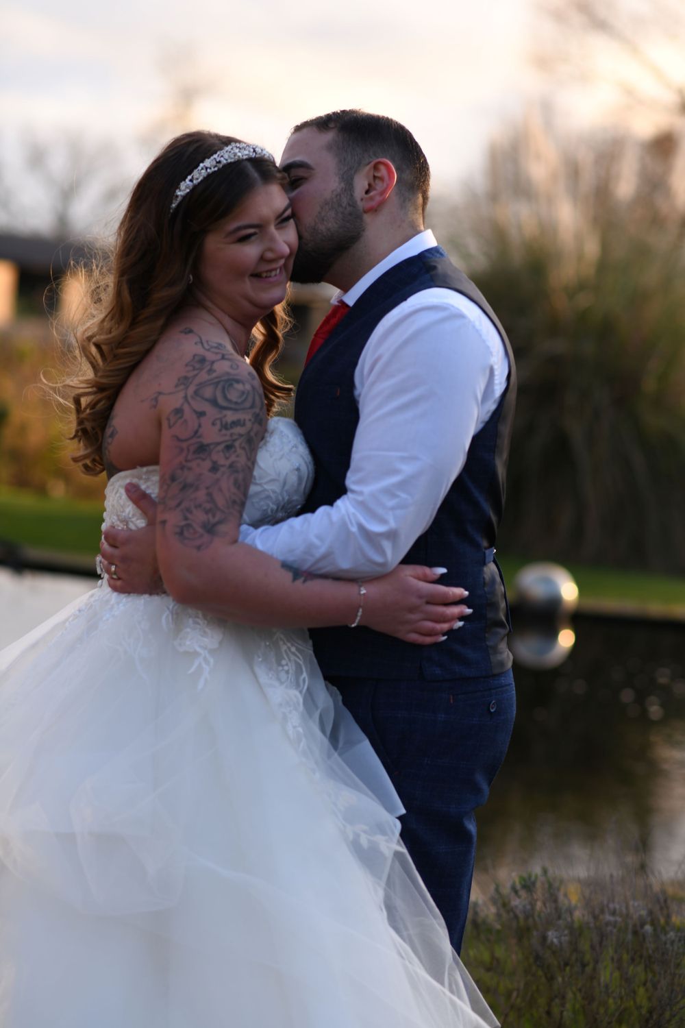 A romantic sunset wedding photo with the couple sharing an intimate embrace by a pond.