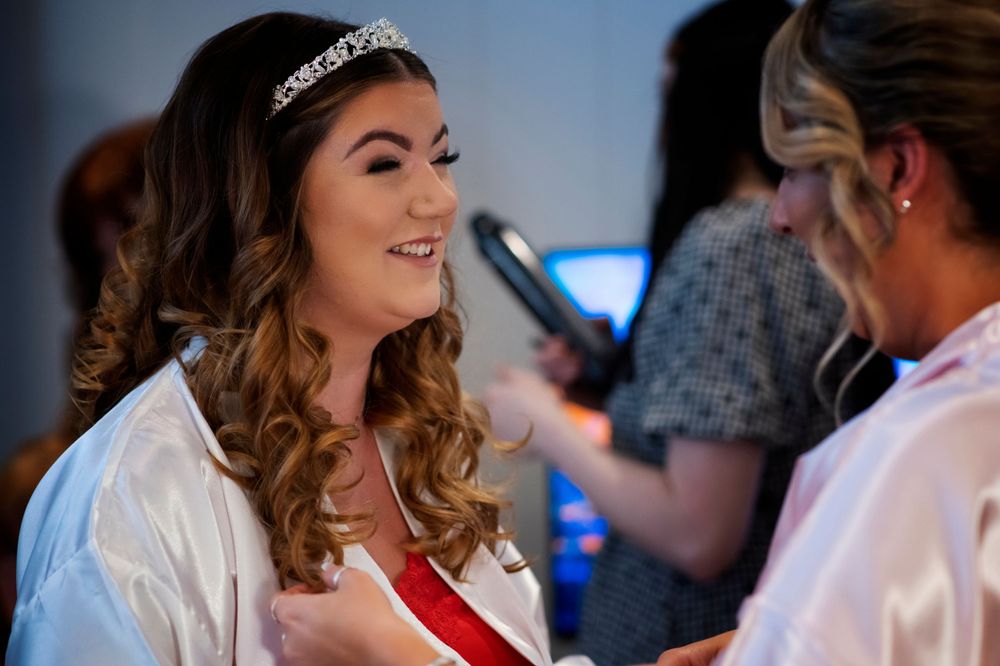 Bride getting ready in white robe with curled hair and tiara during wedding preparations.