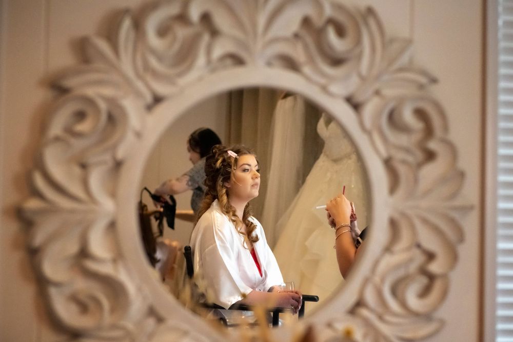 Bride's reflection in decorative white mirror during wedding day preparations.