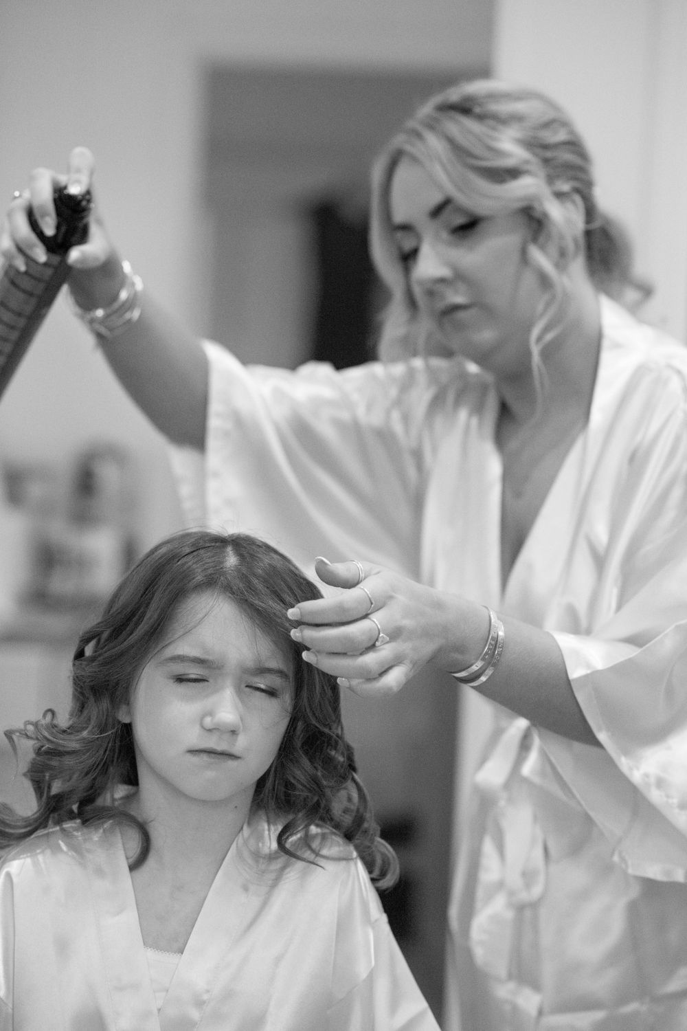 Black and white image of stylist working on bridesmaid's hair during wedding preparations.