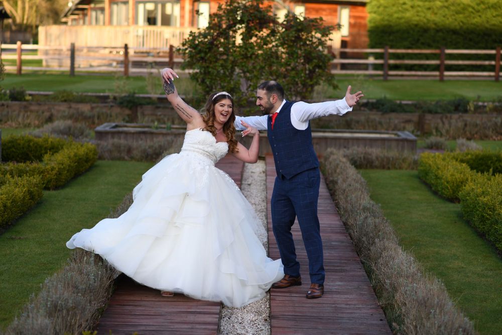 Joyful wedding couple posing playfully on a wooden walkway in a garden setting.