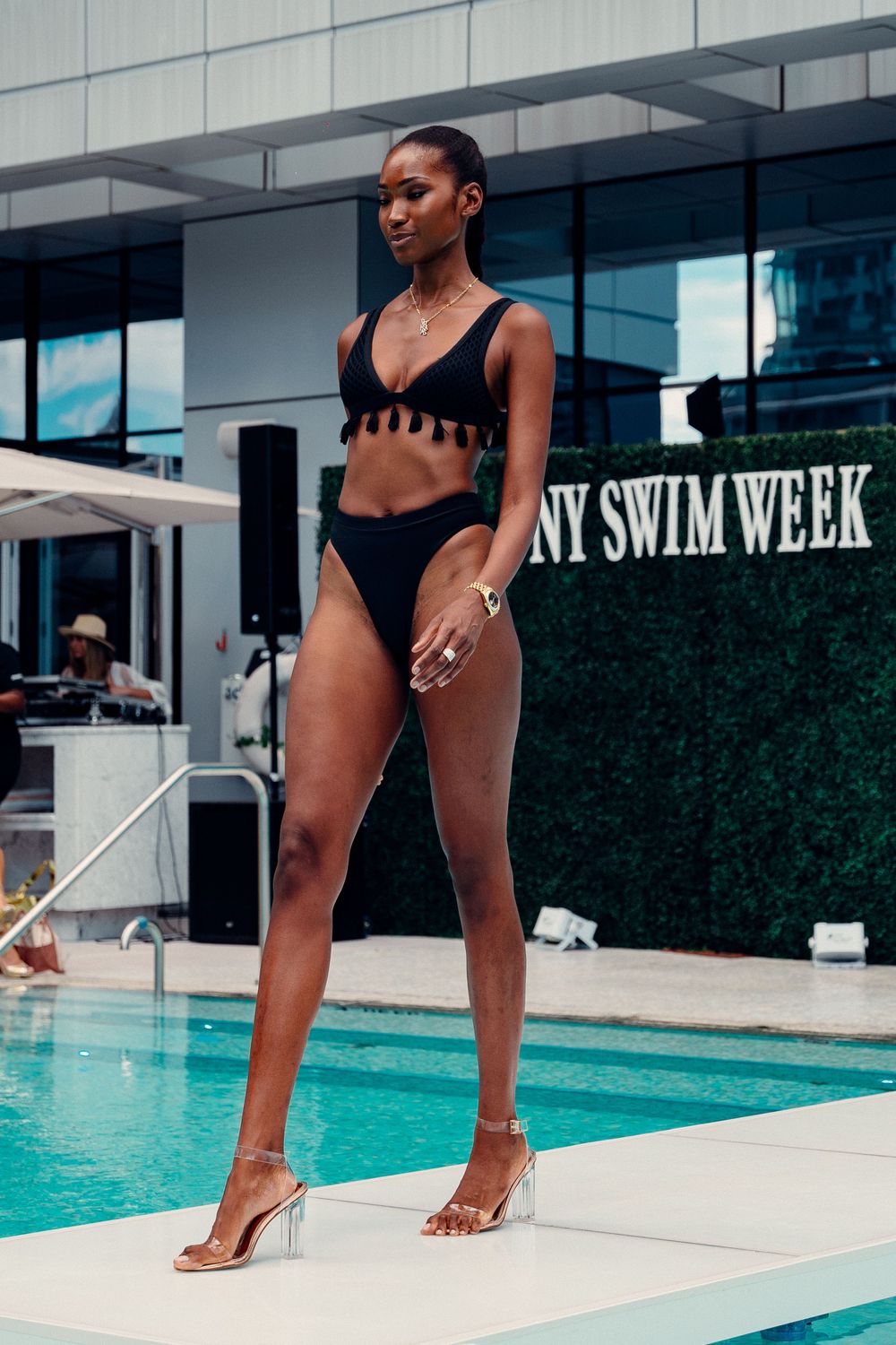 A model in a black swimsuit posing by a luxurious pool during a swimwear photoshoot.
