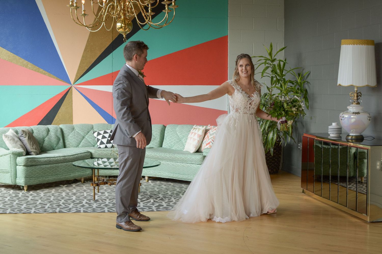 Newlyweds share their first dance in a modern room with colorful geometric wall art and mint green couch.