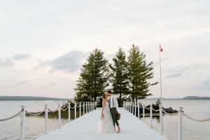 A couple walks along a white dock and evergreen trees on a cloudy summer evening-Northridge Inn-Alexis Anne Photography