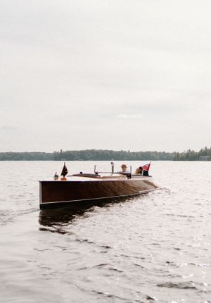 Vintage wooden motorboat with classic design glides across a serene lake on an overcast day-Muskoka Wedding-Alexis Anne Photography
