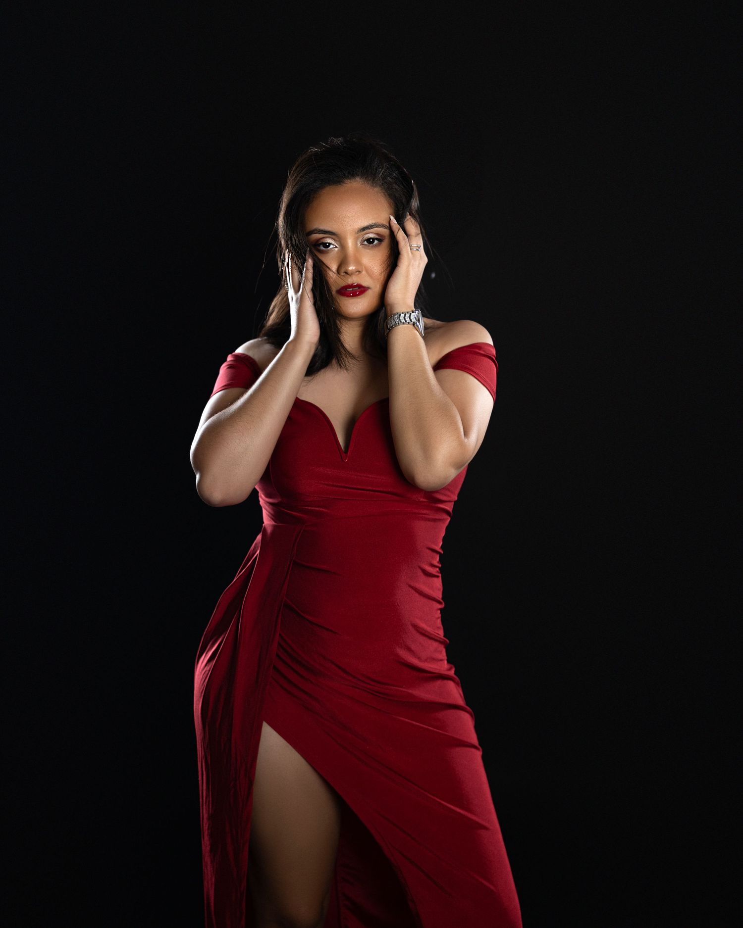 Glamour portrait against dark background featuring model in elegant red evening gown.