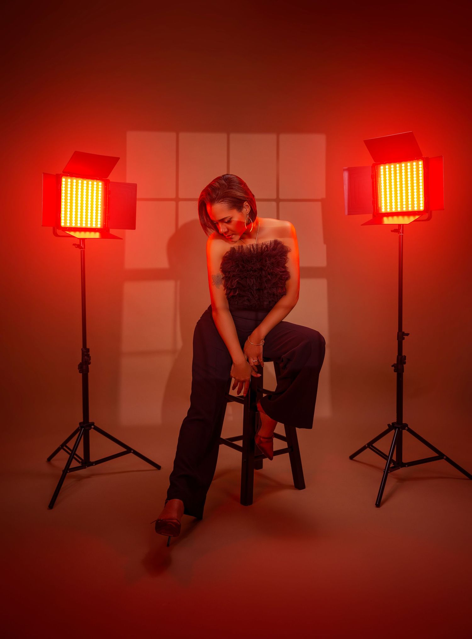 Dramatic portrait in red lighting with two LED panels illuminating figure seated on stool in dark setting.