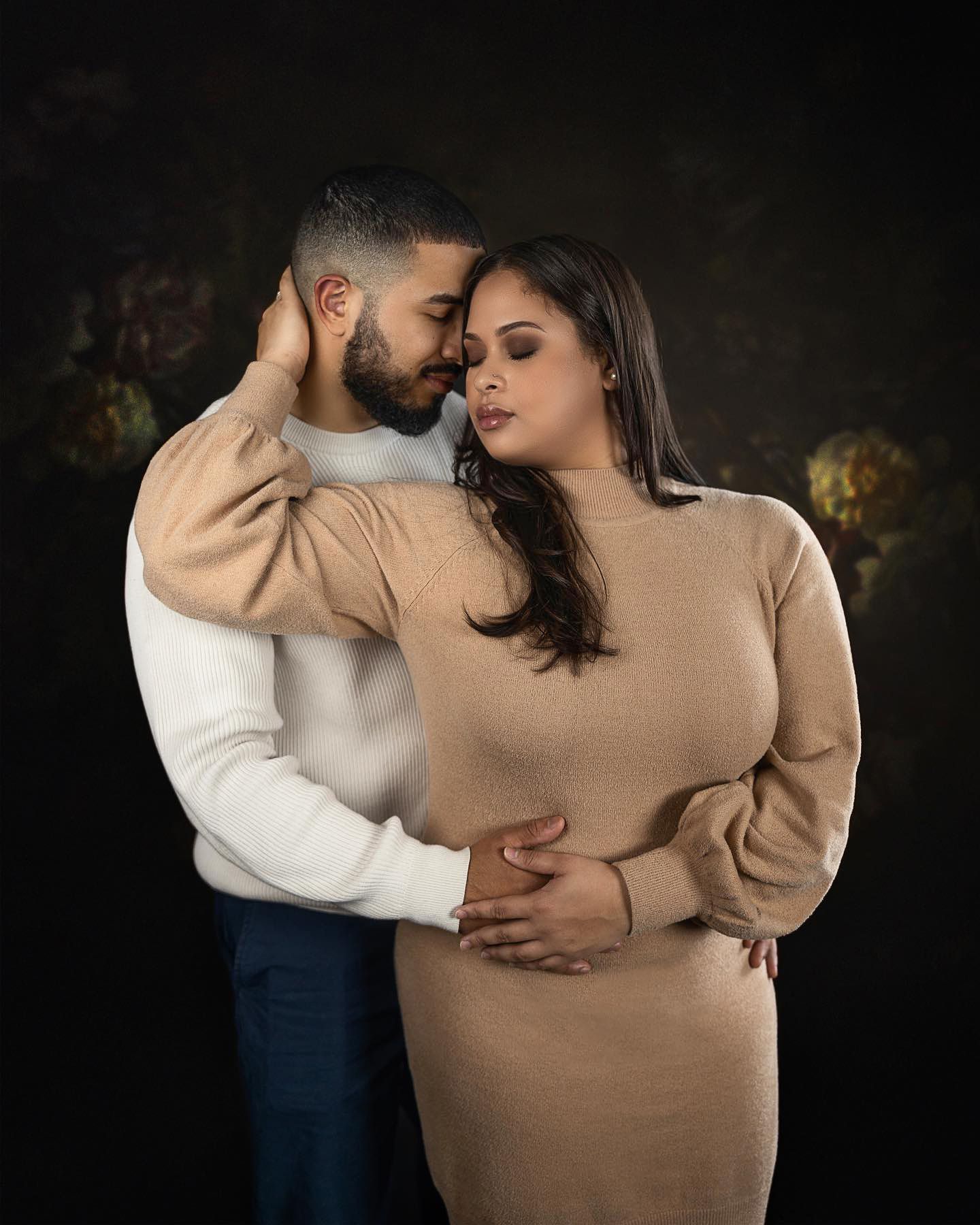 Intimate couple portrait in neutral toned sweaters against dark background.