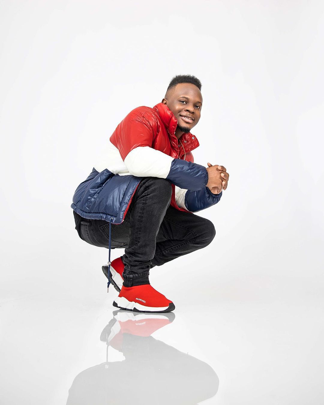 Athletic pose in red and white jacket with blue backpack against white studio background.
