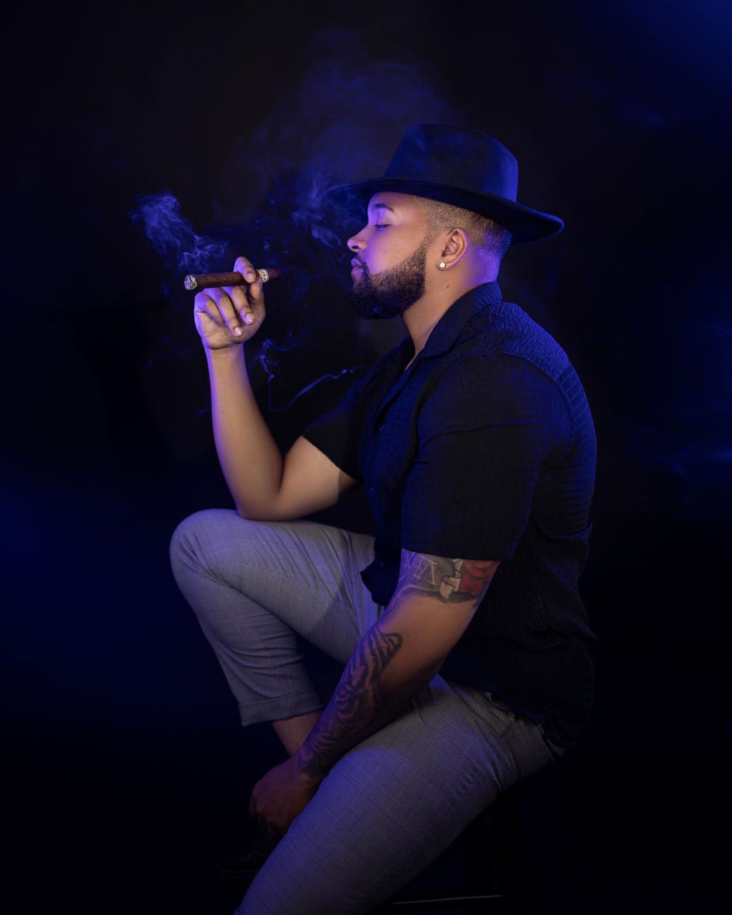 Performer in black hat and outfit singing in dramatic lighting on dark stage.