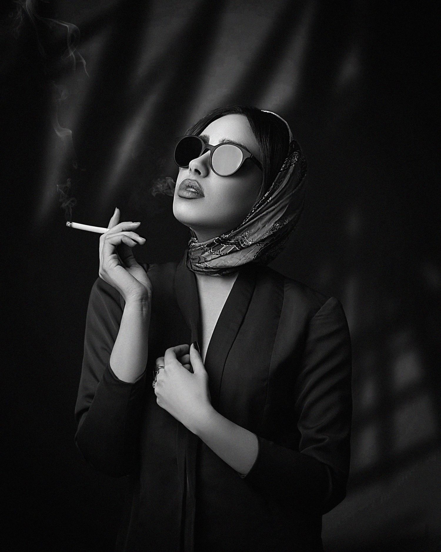 Stylish portrait of person in hijab and sunglasses smoking against dark background.
