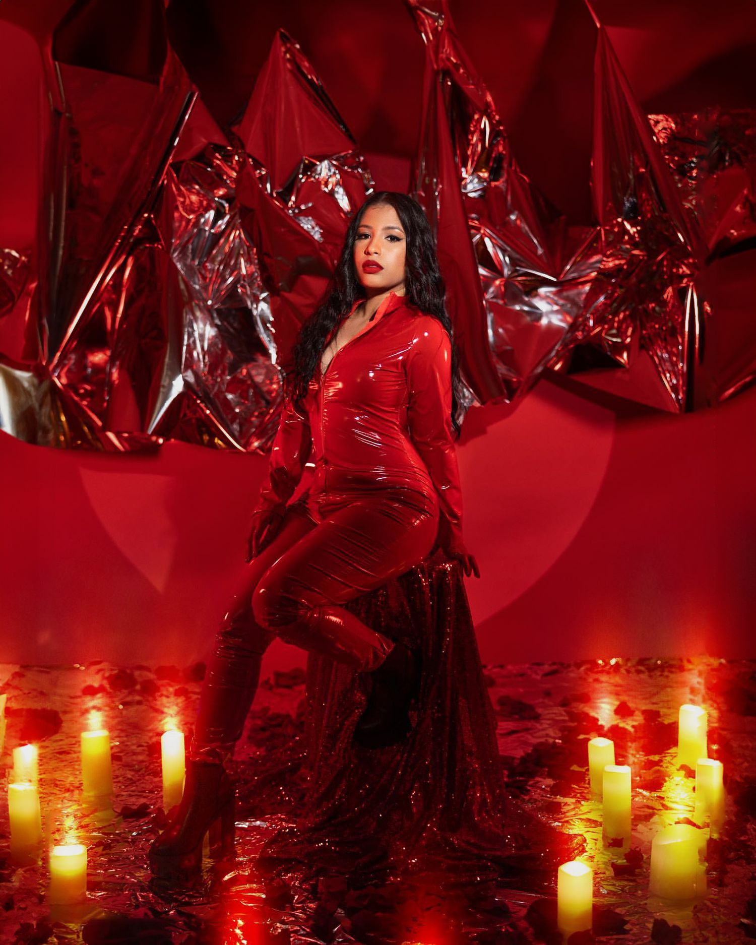 Fashion portrait in red latex outfit surrounded by metallic decorations and candles.