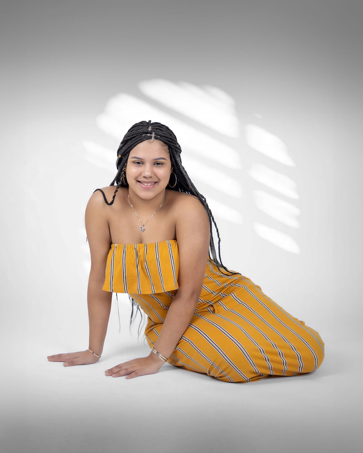 Model in yellow striped outfit poses on white backdrop with window shadows.