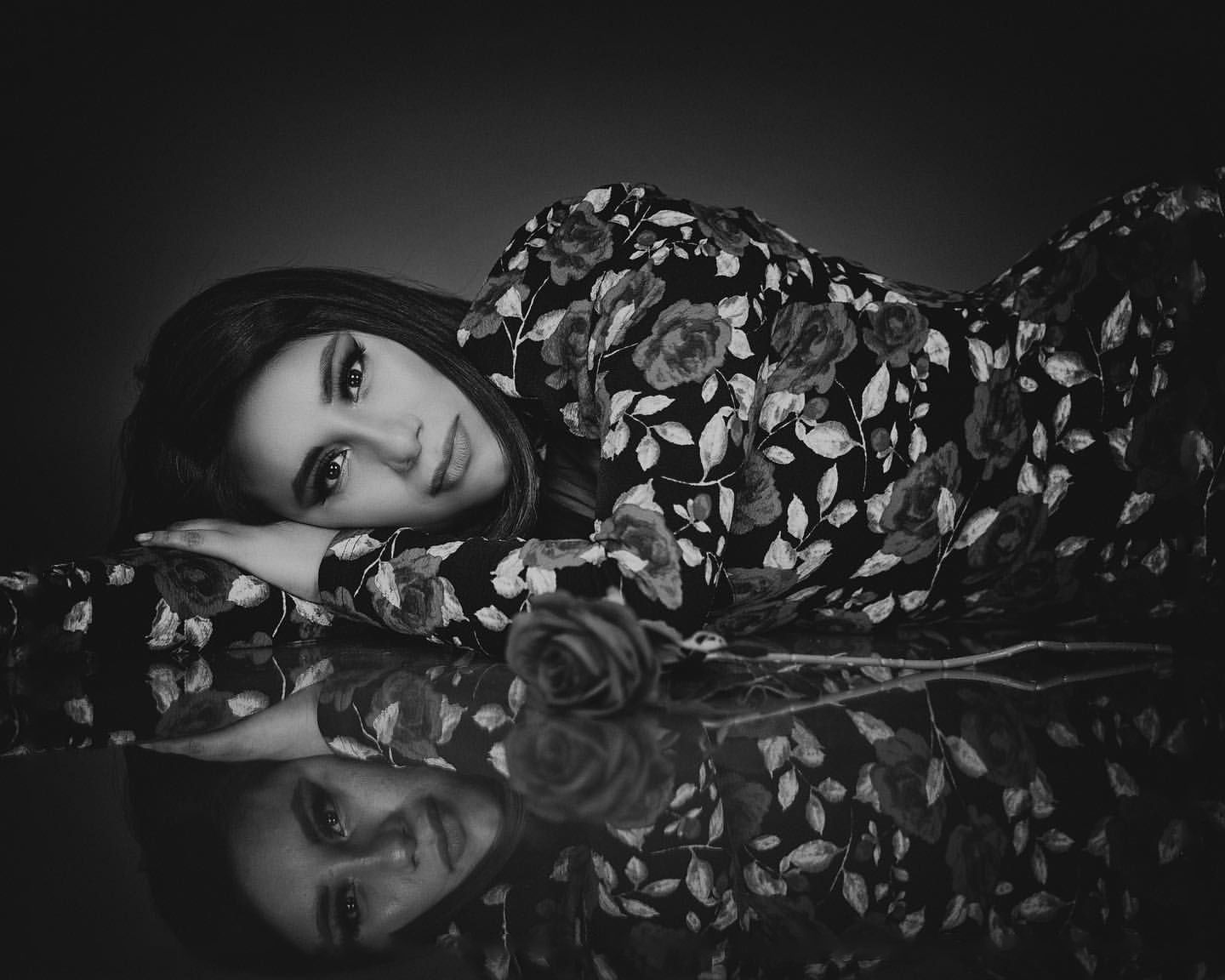 Artistic black and white portrait with reflective surface creating mirror effect of floral pattern dress.