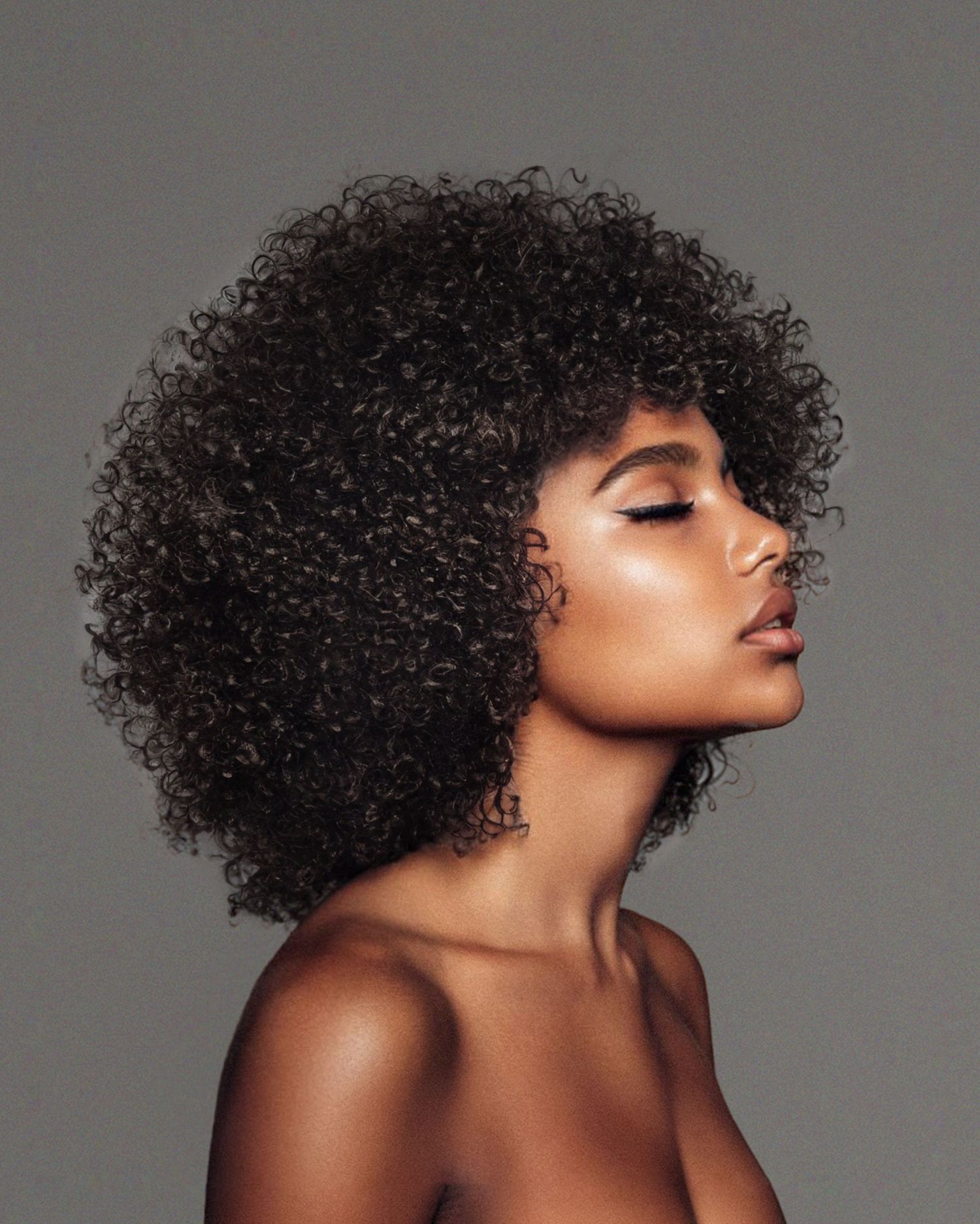 Beauty portrait highlighting natural curly afro hairstyle against neutral background.